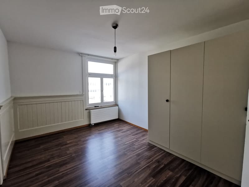 Empty room with wooden flooring, white walls, a window with white frame, radiator, and a built-in closet.