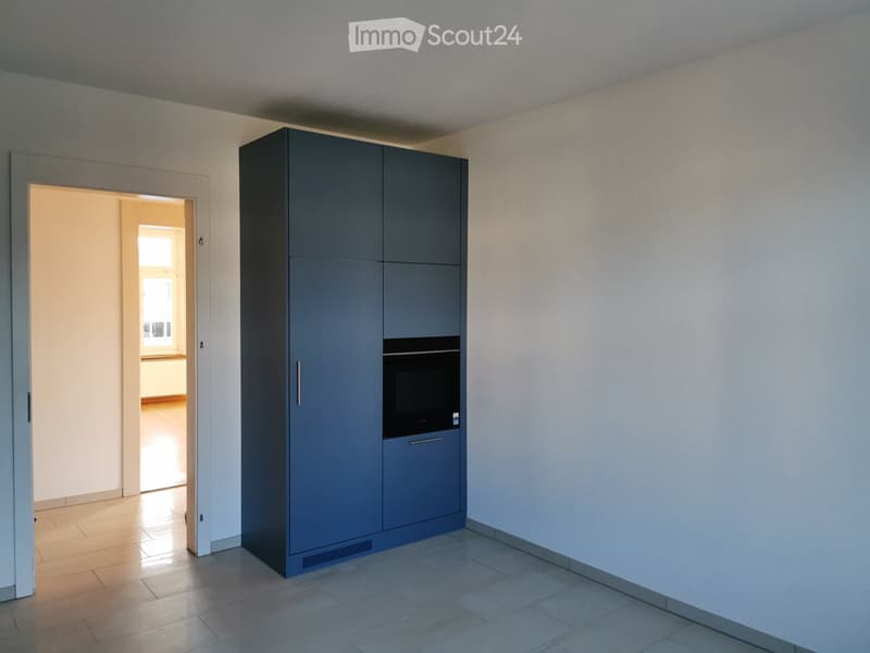 Modern kitchen with grey cabinetry, built-in oven, tiled floor, and open doorway leading to another room.