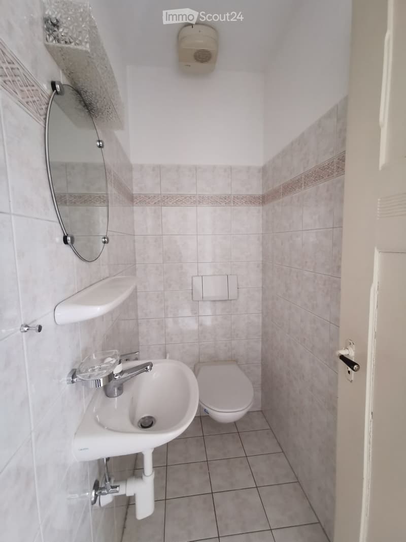Modern bathroom with a white sink, chrome faucet, toilet, wall-mounted mirror, and a towel on a rack.