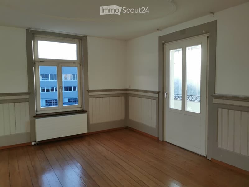 Empty room with wooden flooring, white walls, a window with a radiator below, and a door with glass panels leading to another space.