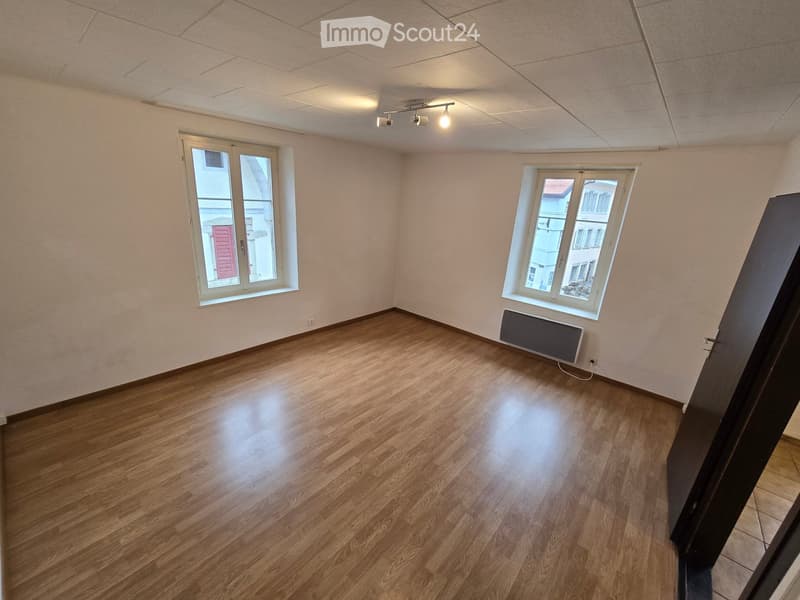 Empty room with wooden flooring, white walls, two windows, and a radiator. No furniture or equipment present.