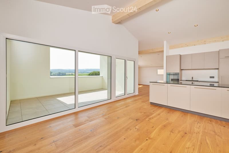 Modern kitchen with light-colored cabinets, a sink, and an oven, connected to a spacious living area with large glass doors leading to a balcony.