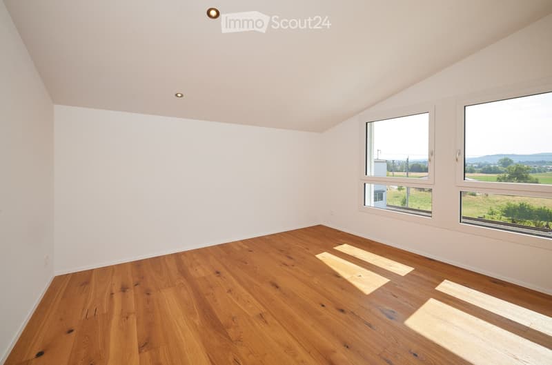 Empty room with wooden flooring and white walls, featuring large windows offering a scenic view of the countryside.