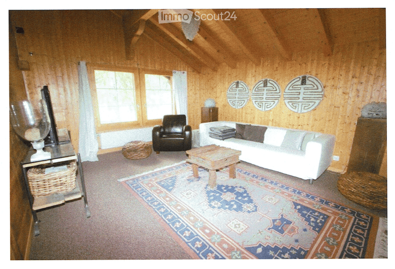 Cozy living room with wooden walls and ceiling, large windows, white sofa, dark armchair, wooden coffee table, and decorative mirrors.