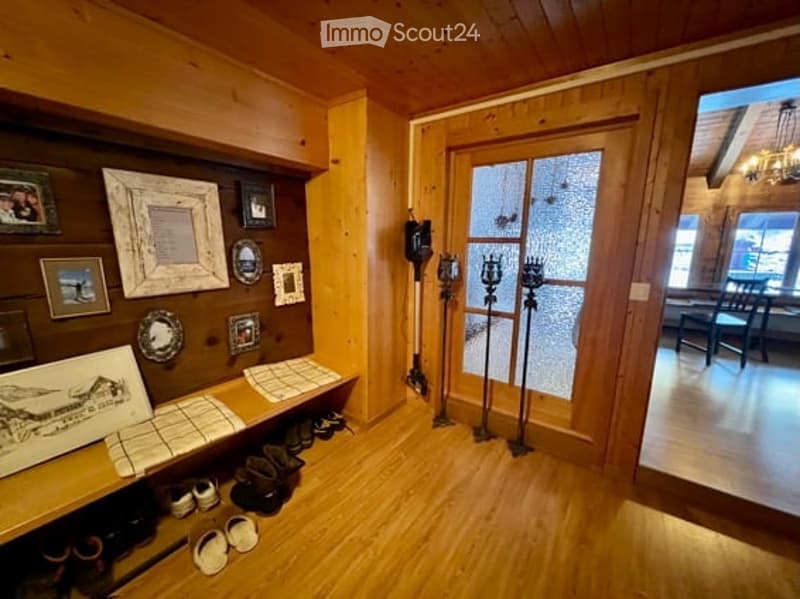 Wooden hallway with a shoe rack, framed pictures on the wall, and an open door leading to another room.
