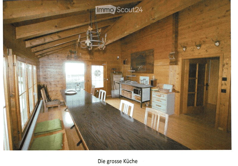 A spacious, wooden-paneled dining area with a long wooden dining table surrounded by chairs, a small kitchen area with cabinets and a microwave, and a chandelier hanging from the ceiling.