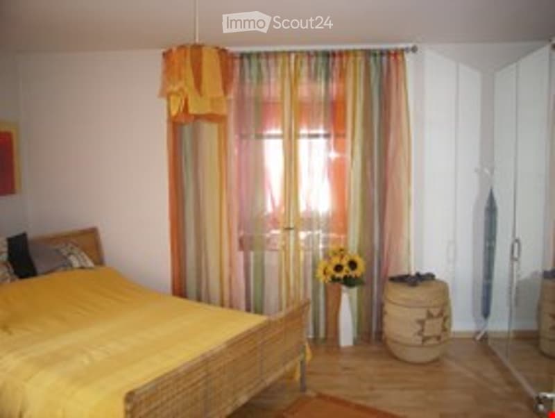 Cozy bedroom with a wooden bed, yellow bedding, colorful striped curtains, a flower vase on the floor, and a wardrobe.