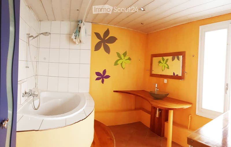 Bright bathroom with a white bathtub, wooden sink counter, and a mirror with floral designs on the walls.