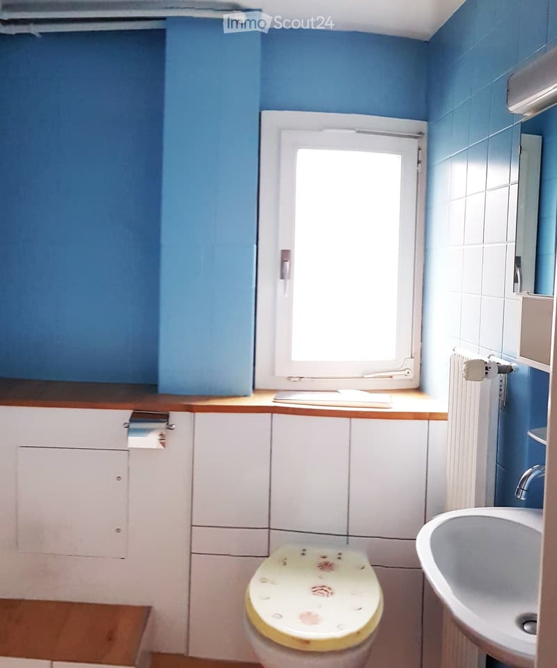 Bathroom with blue walls, white tiled section, wooden countertop, toilet, sink, and radiator.