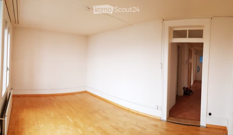Empty room with light wooden flooring and white walls, featuring a large window and a doorway leading to another area.
