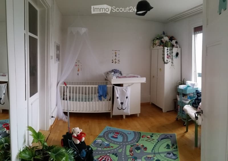 Brightly lit children's bedroom with a crib, toy car, plush toy, play mat, cabinet, and decorative items.
