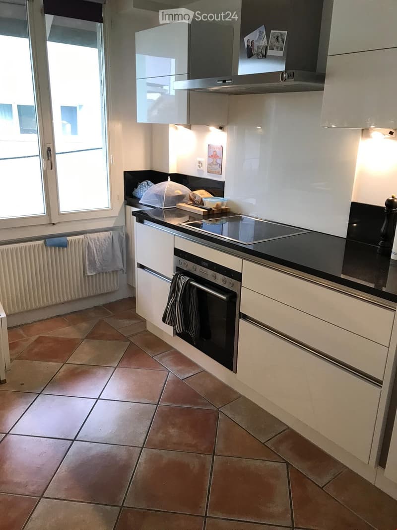 Modern kitchen with white cabinets, black countertops, induction stove, oven, and tiled floor.