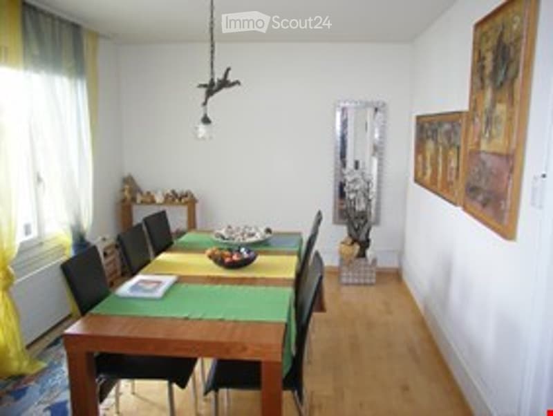 Dining room with wooden floor, large dining table, six chairs, mirror, and artwork on the wall.