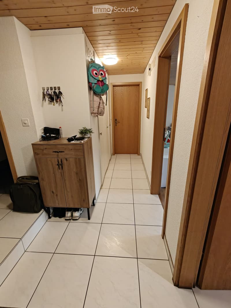 A narrow hallway with tiled flooring, wooden doors, and a small wooden cabinet with keys and a backpack hanging on the wall.