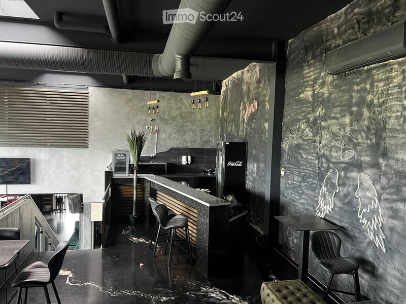 Modern bar area with dark stone walls, sleek bar counter, bar stools, tables, chairs, and a refrigerator.
