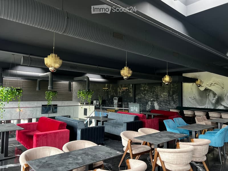 Modern lounge area with dark walls, pendant lights, colorful sofas, tables, and chairs arranged for seating.