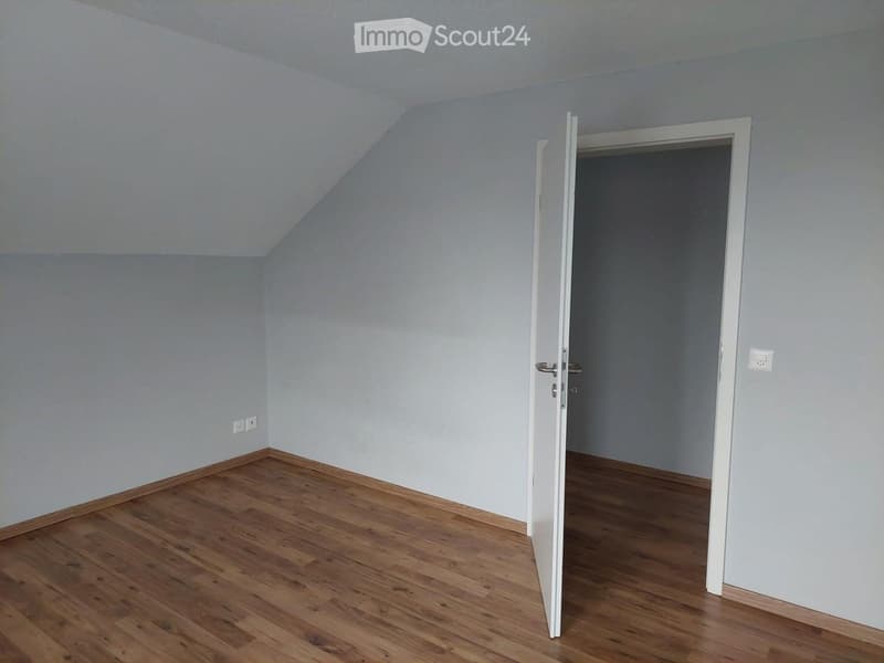 Empty room with wooden flooring, light grey walls, and an open door leading to another room.