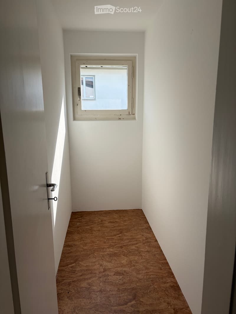 Empty hallway with white walls, wooden floor, and a single window at the far end.