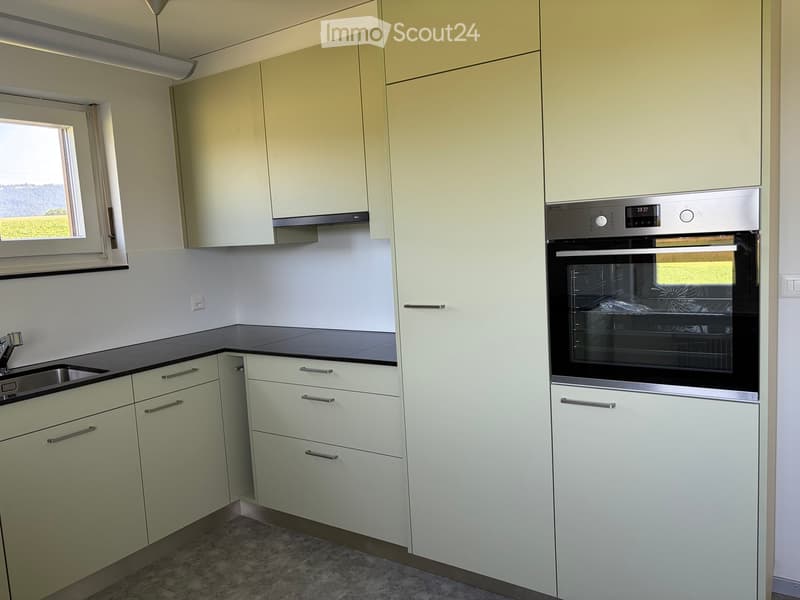Modern kitchen with light-colored cabinets, a black countertop, a stainless steel oven, and a sink with a faucet.