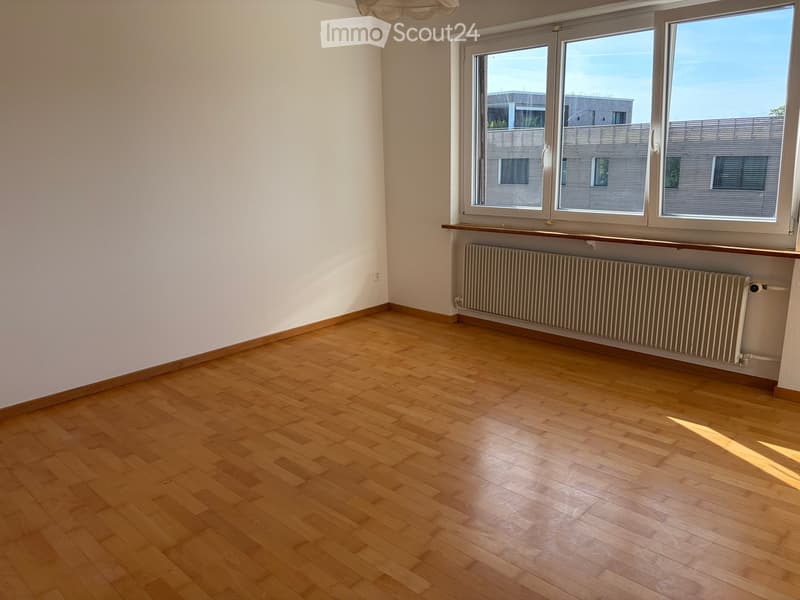 Empty room with wooden flooring, white walls, large windows, radiator, and a small shelf under the windows.