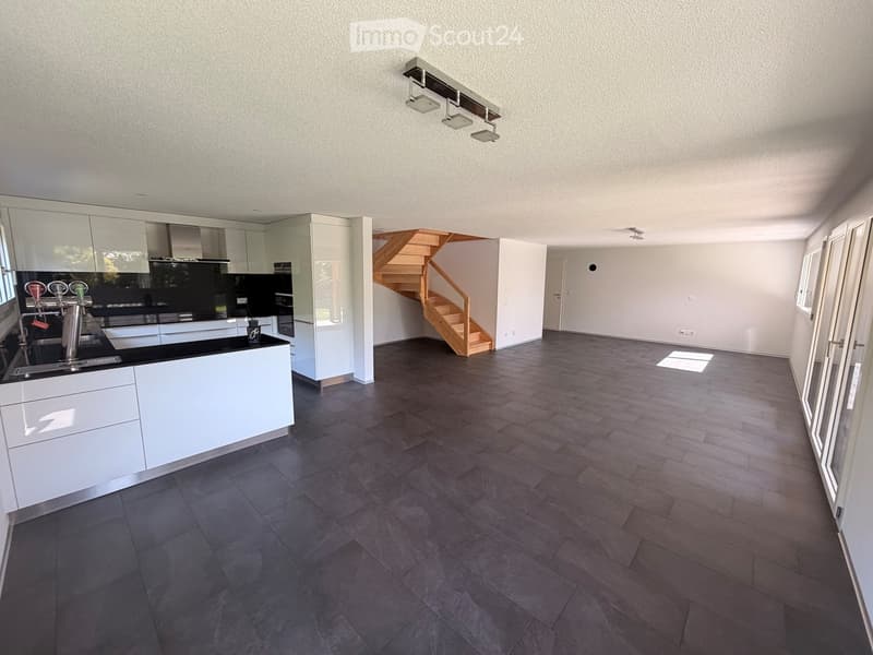 modern kitchen with white cabinets, black countertops, wooden staircase, large windows, tiled floor