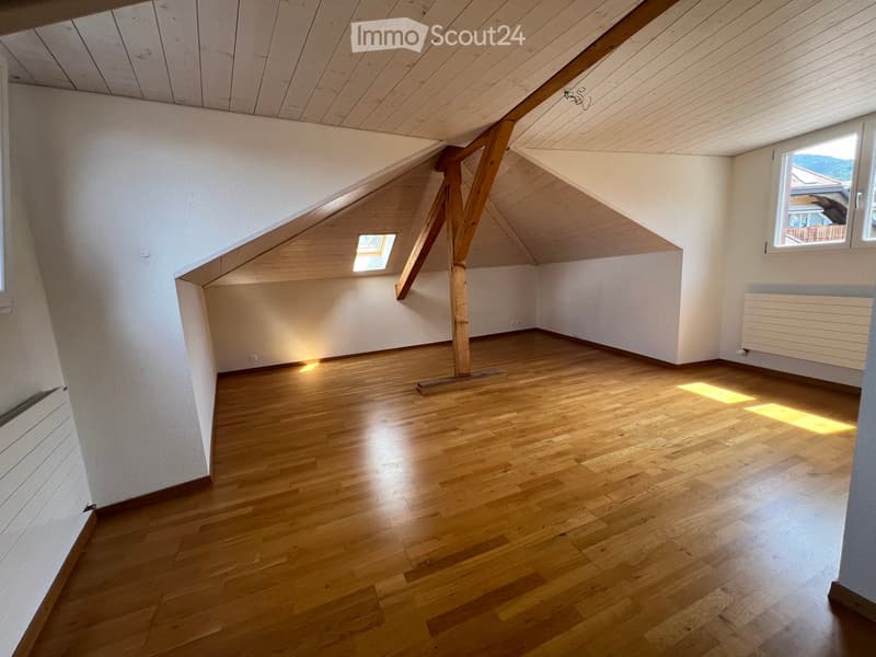 Empty attic room with wooden floors, white walls, exposed wooden beams, and skylight windows allowing natural light.