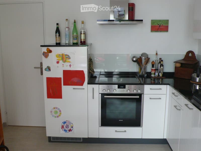 Modern kitchen with white cabinets, stainless steel oven, refrigerator adorned with colorful magnets, and various bottles on the counter.