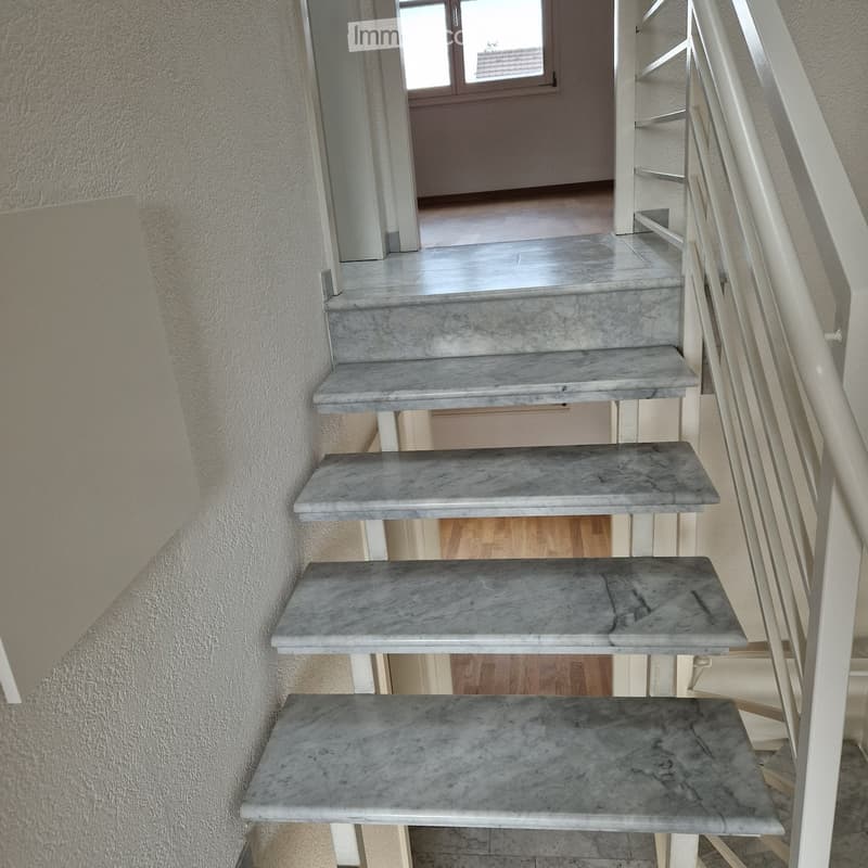 Staircase with marble steps and white metal railing, leading to an open area with wooden flooring and a window at the end.
