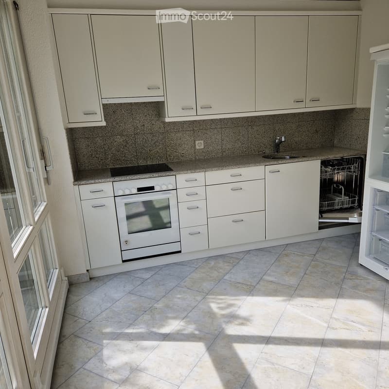 Modern kitchen with white cabinets, granite countertops, and tiled floor. Features an oven, dishwasher, and refrigerator.