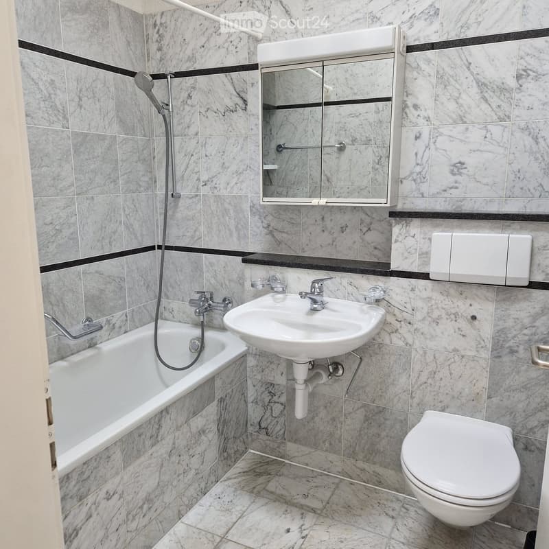 Modern bathroom with marble tiles, a bathtub, a sink, a toilet, a mirror, and a showerhead.
