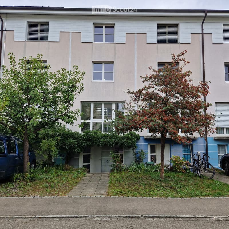 Two-story residential building with light-colored facade, multiple windows, and small garden area in front.