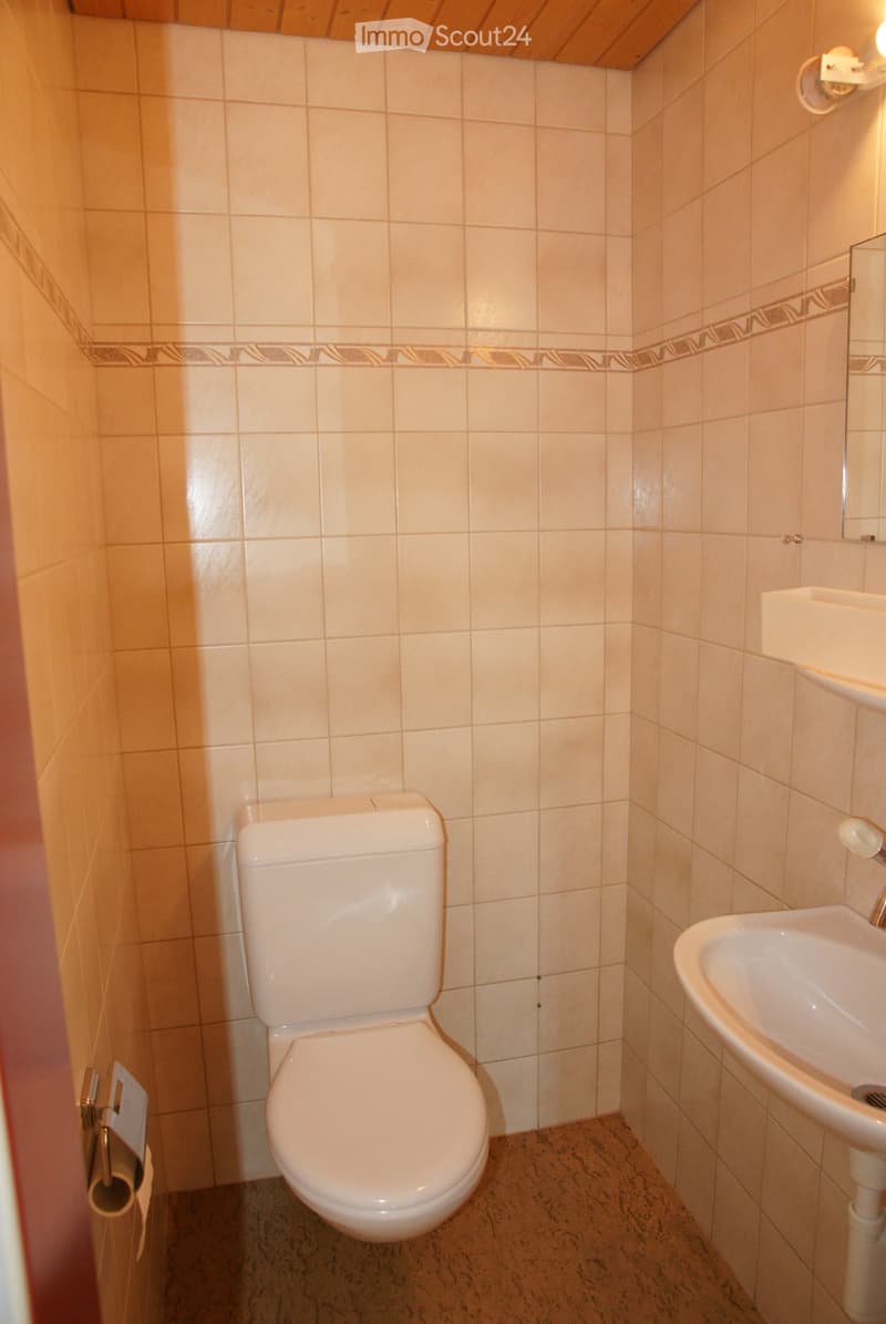 Small bathroom with beige tiled walls, a white toilet, a white sink, and a toilet paper holder. The floor is made of dark marble tiles.