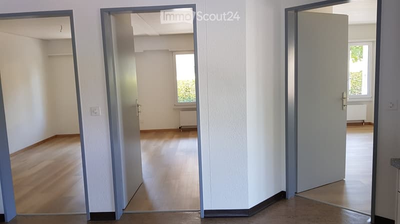 Empty hallway with wooden flooring, white walls, and open doors leading to adjacent rooms. No furniture or equipment visible.