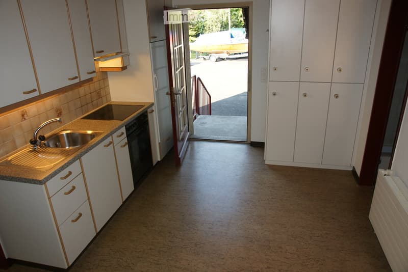 Modern kitchen with white cabinets, granite countertop, stainless steel sink, and built-in oven. Open doorway leads to outdoor area.