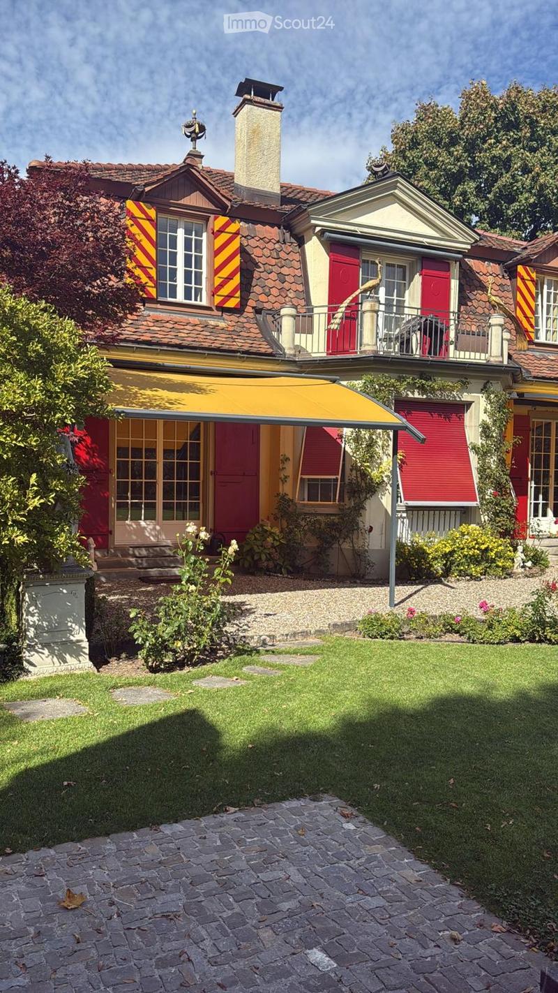 Cobblestone driveway, Red roof, Red and yellow shutters, yellow awning, large tree in front of the house, brick pavement