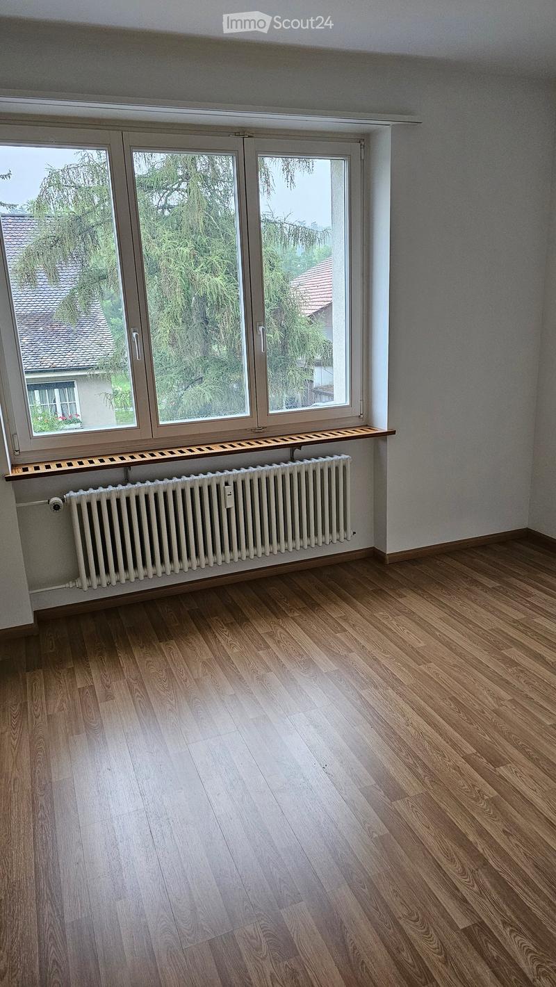 Empty room with wooden flooring, large windows, radiator, and a small shelf under the windows.