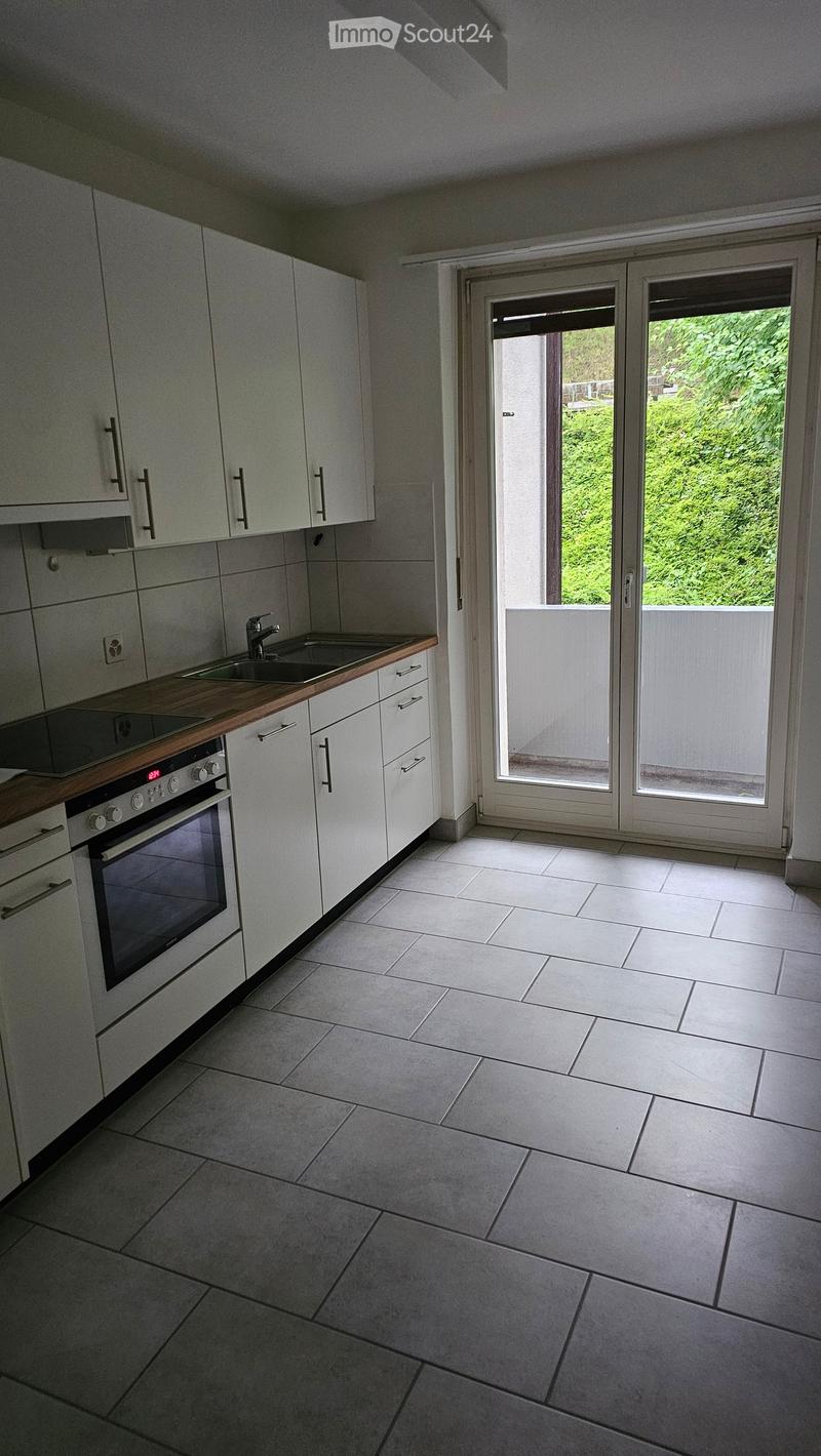 Modern kitchen with white cabinets, a sink, and an oven. The space features tiled flooring and large windows leading to a balcony.