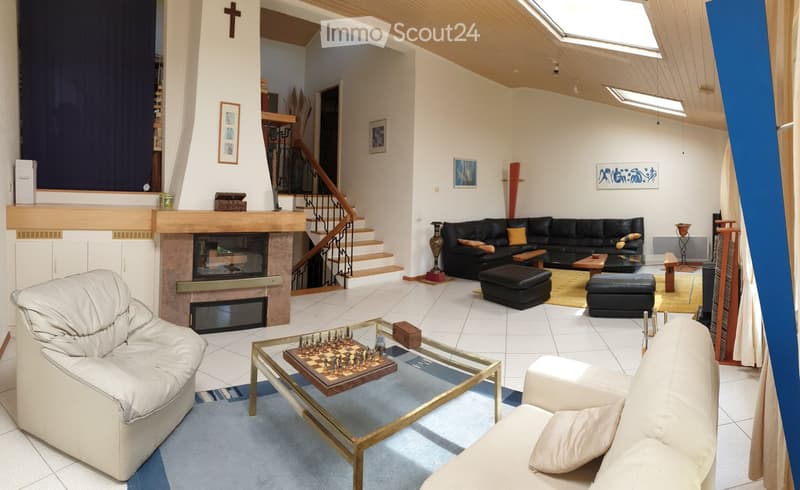 Modern living room with a fireplace, white leather chairs, a black sectional sofa, glass coffee table, and chessboard on the table.