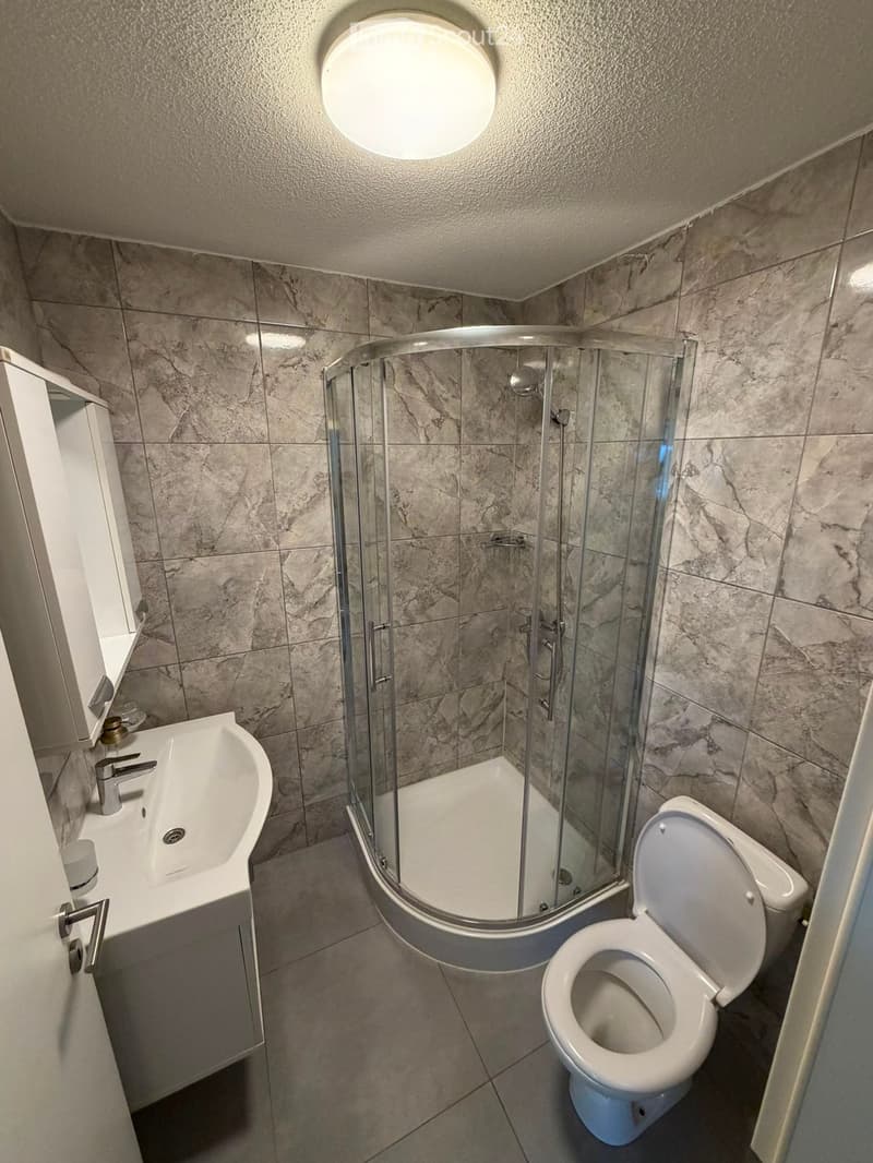 Modern bathroom with marble tiles, a white sink with a chrome faucet, a toilet, and a glass-enclosed shower stall.