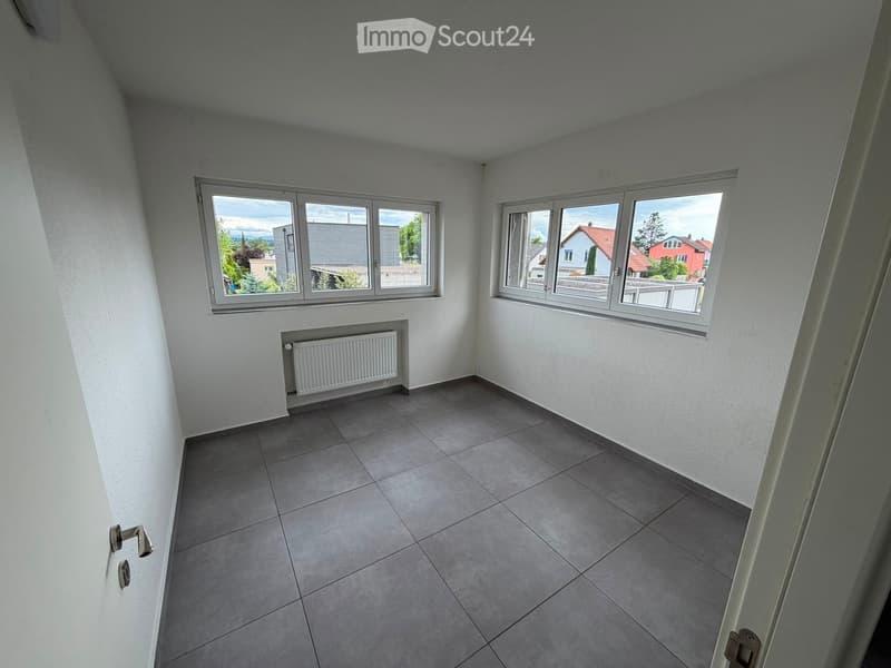 Empty room with tiled floor, white walls, large windows, and a radiator. No furniture or equipment present.