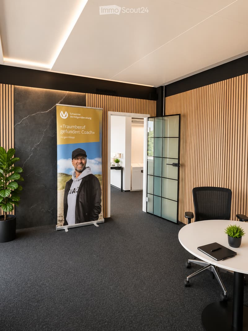 Modern office space with a round table, office chair, potted plant, and a large screen displaying a promotional image.