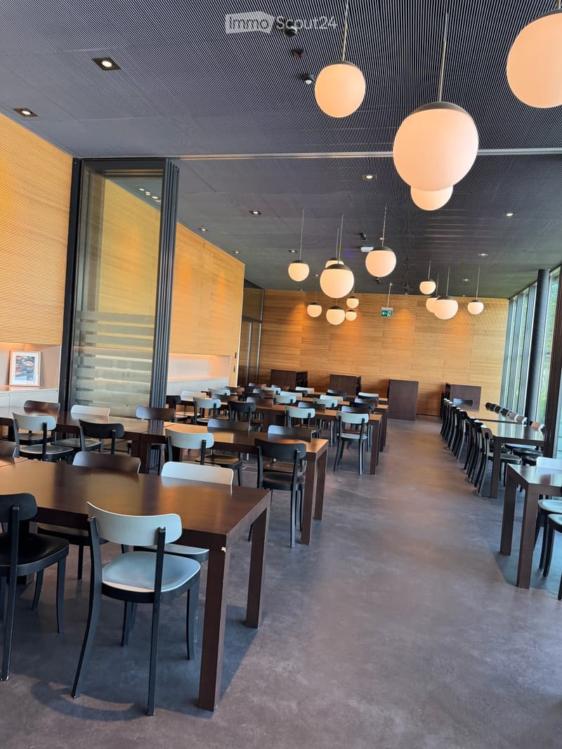 Modern dining area with multiple tables and chairs arranged in rows, large pendant lights, and a sleek, contemporary design with wooden paneling and glass walls.
