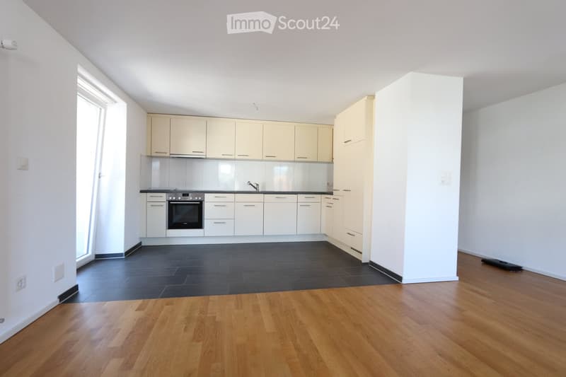 Modern kitchen with white cabinets, black countertop, and a dark tiled floor. The adjacent area features wooden flooring.