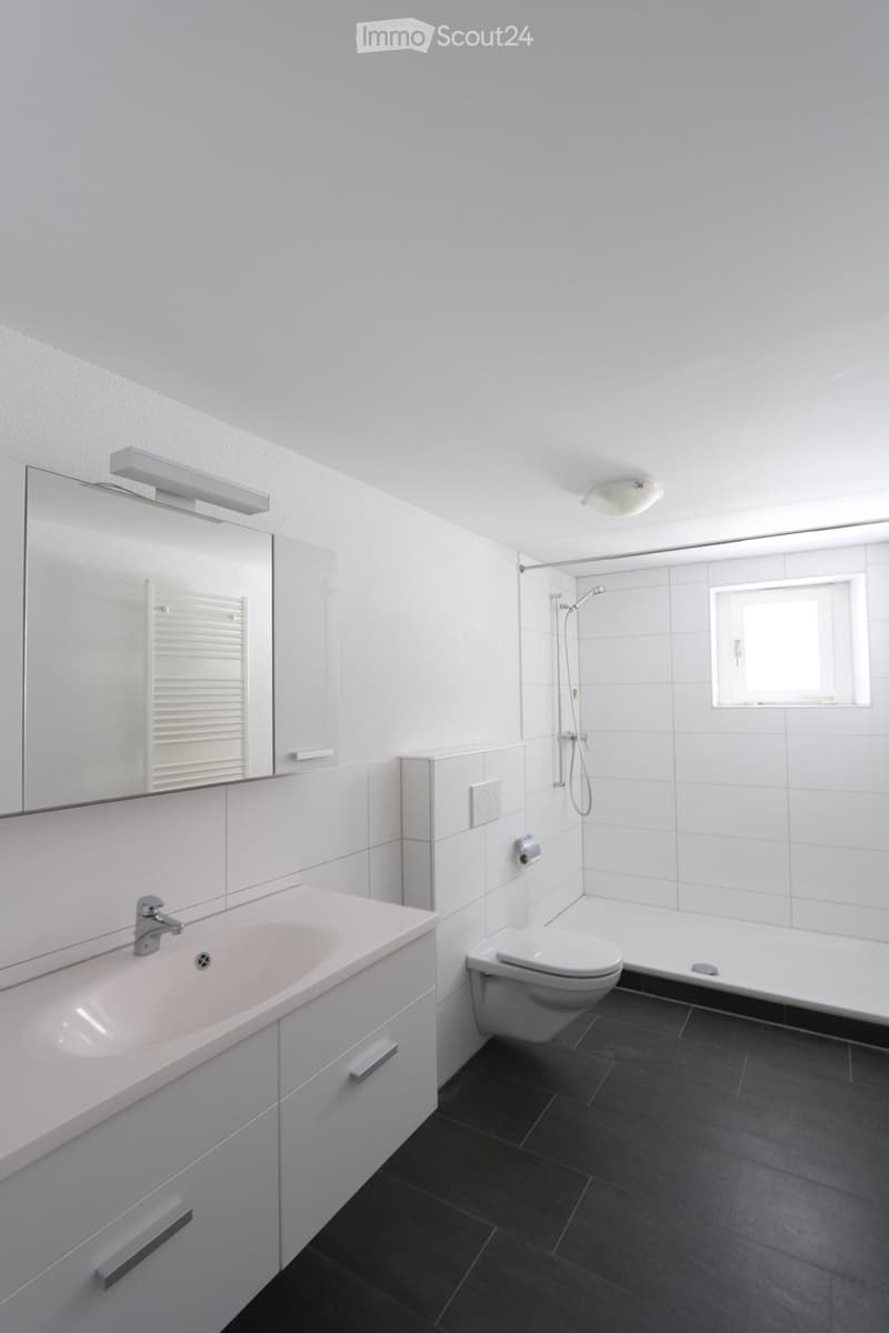 Modern bathroom with white tiles, a sink with a mirror, a toilet, a bathtub, and a shower area with a window.