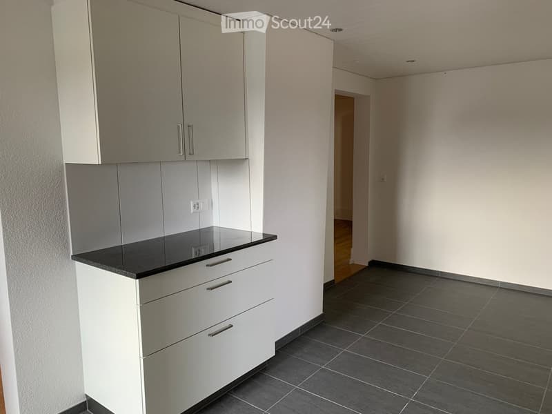Empty kitchen area with white cabinets, black countertop, and dark tiled floor. No appliances or furniture present.