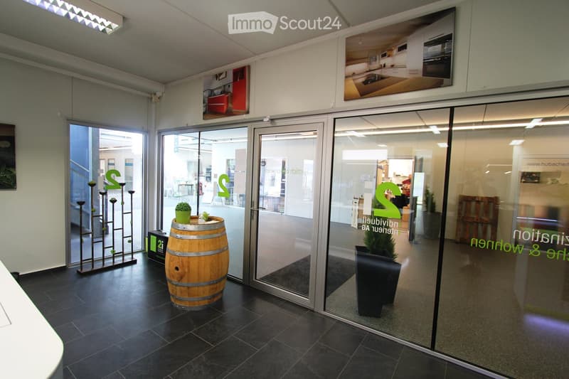 Modern reception area with dark tiled floor, glass doors leading to another room, a wooden wine barrel as a centerpiece, potted plants, and decorative shelves.