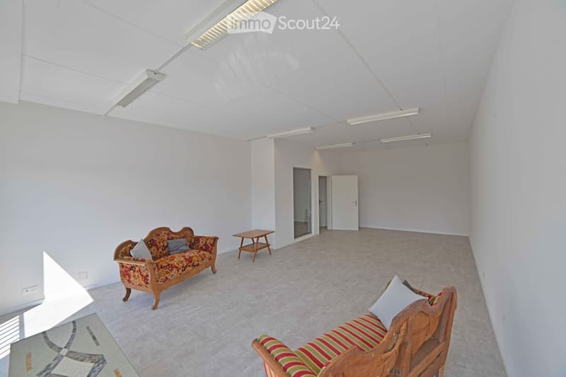 Bright living room with white walls, carpeted floor, two wooden sofas with patterned upholstery, small wooden side table, and glass coffee table.