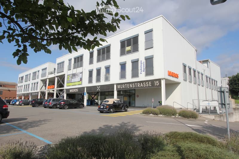 Modern office building with several floors, white exterior, multiple large windows, entrance on Murtenstrasse, underground parking, large parking area in front