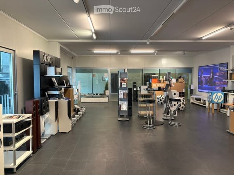 A modern electronics store with various displays including shelves, a large screen, a stool, a chair, and a table.