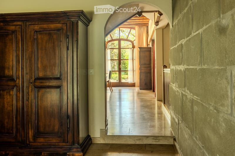 Elegant hallway with arched entryway, polished tile floor, wooden wardrobe, and view to outdoor area through large glass doors.